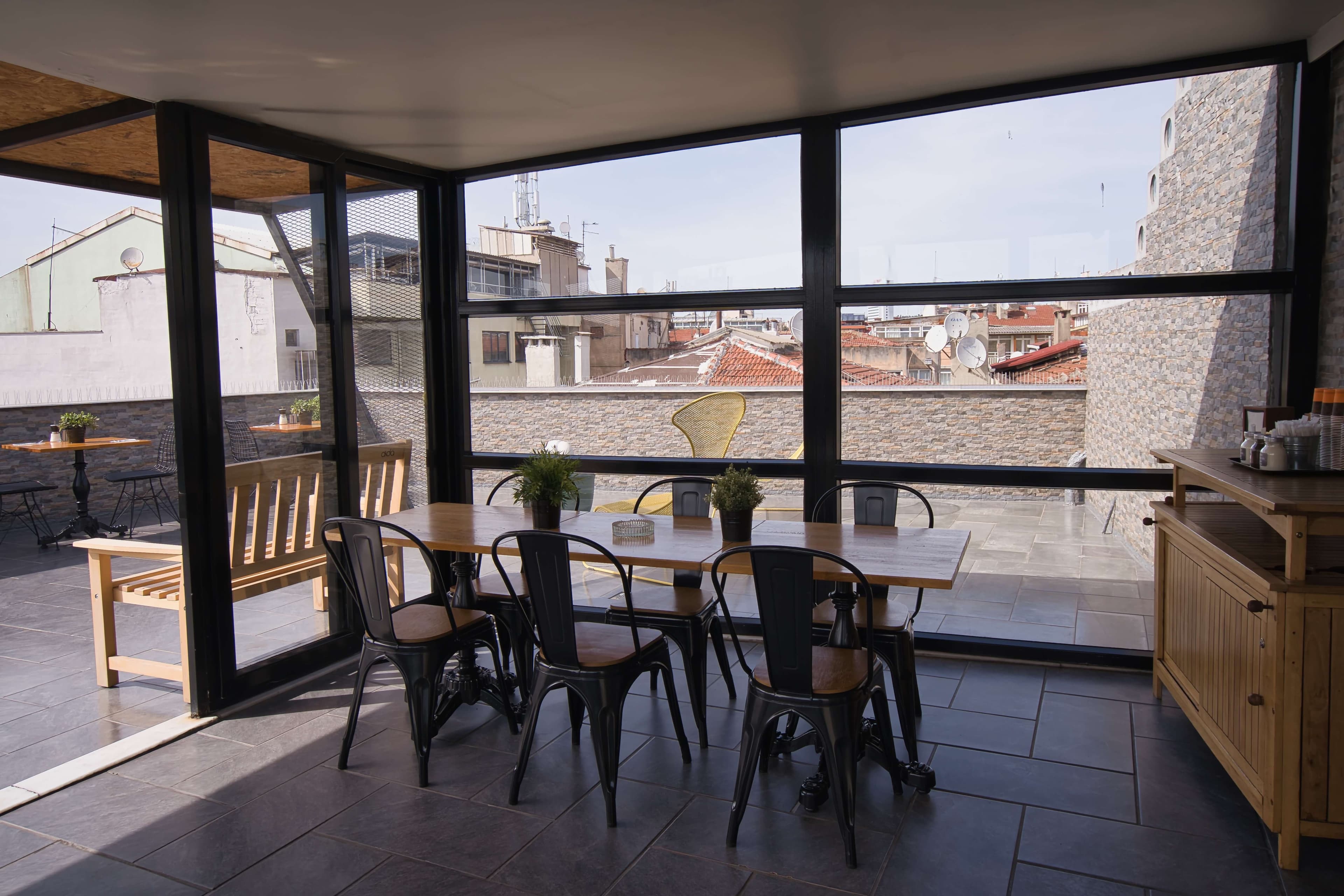 Sunroom dining tables with black metal chairs and rooftop views through the glass