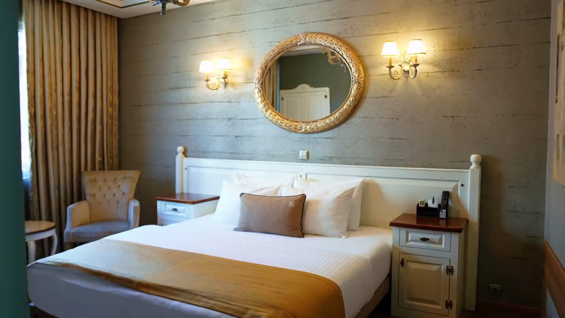 Suite: das Hauptschlafzimmer mit Kingsize-Bett, vergoldetem Ovalspiegel und zwei Wandleuchten