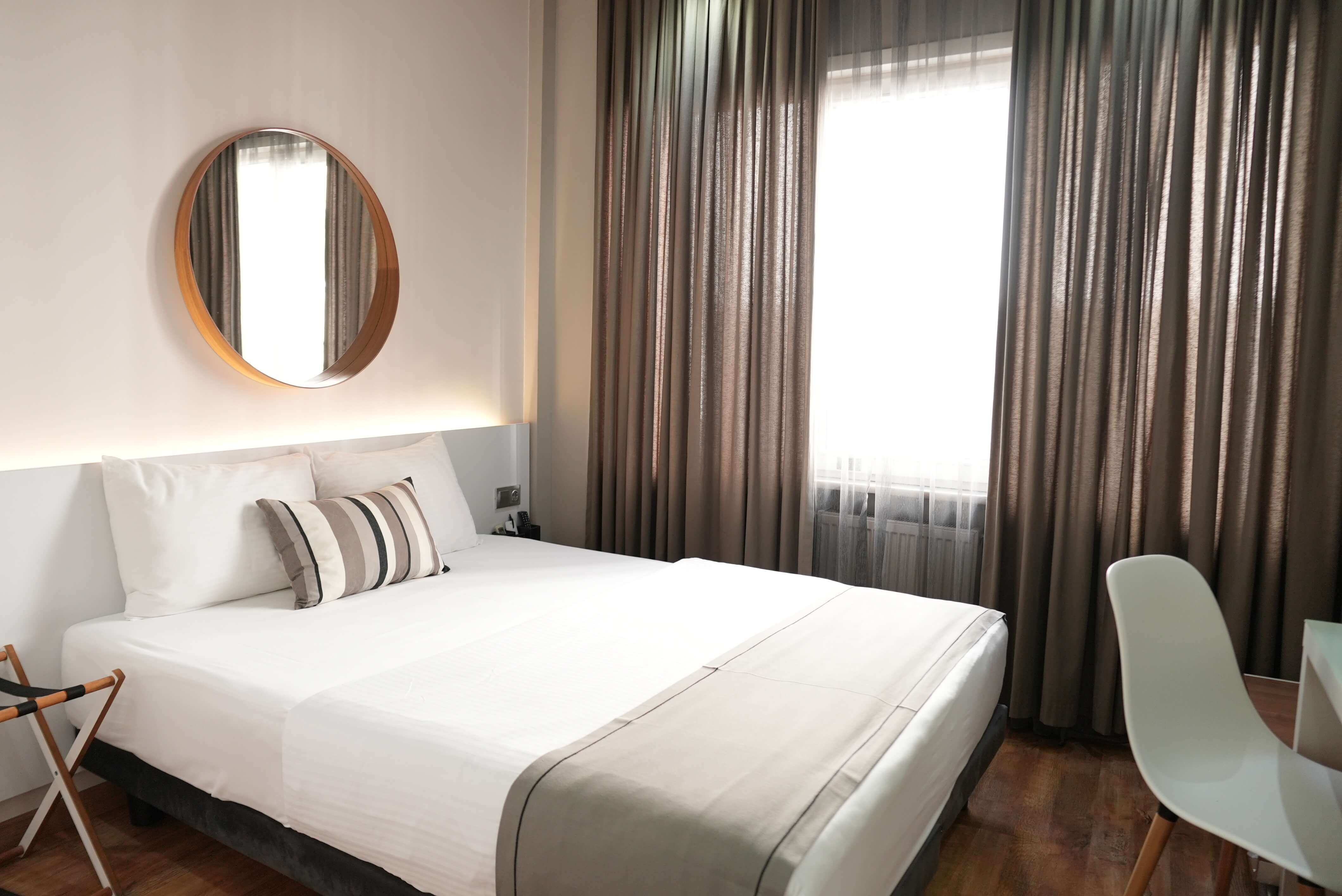 Standard double: double bed under a round mirror, with floor-length curtains and daylight from the window