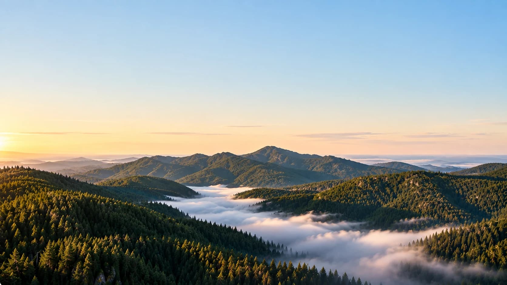 Bewaldete Bergrücken bei Sonnenaufgang, Nebel in den Tälern unter offenem Himmel